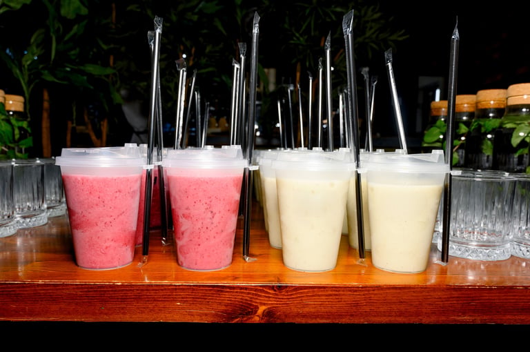 Multiple smoothie cups in pink and yellow colors with straws arranged on a wooden table