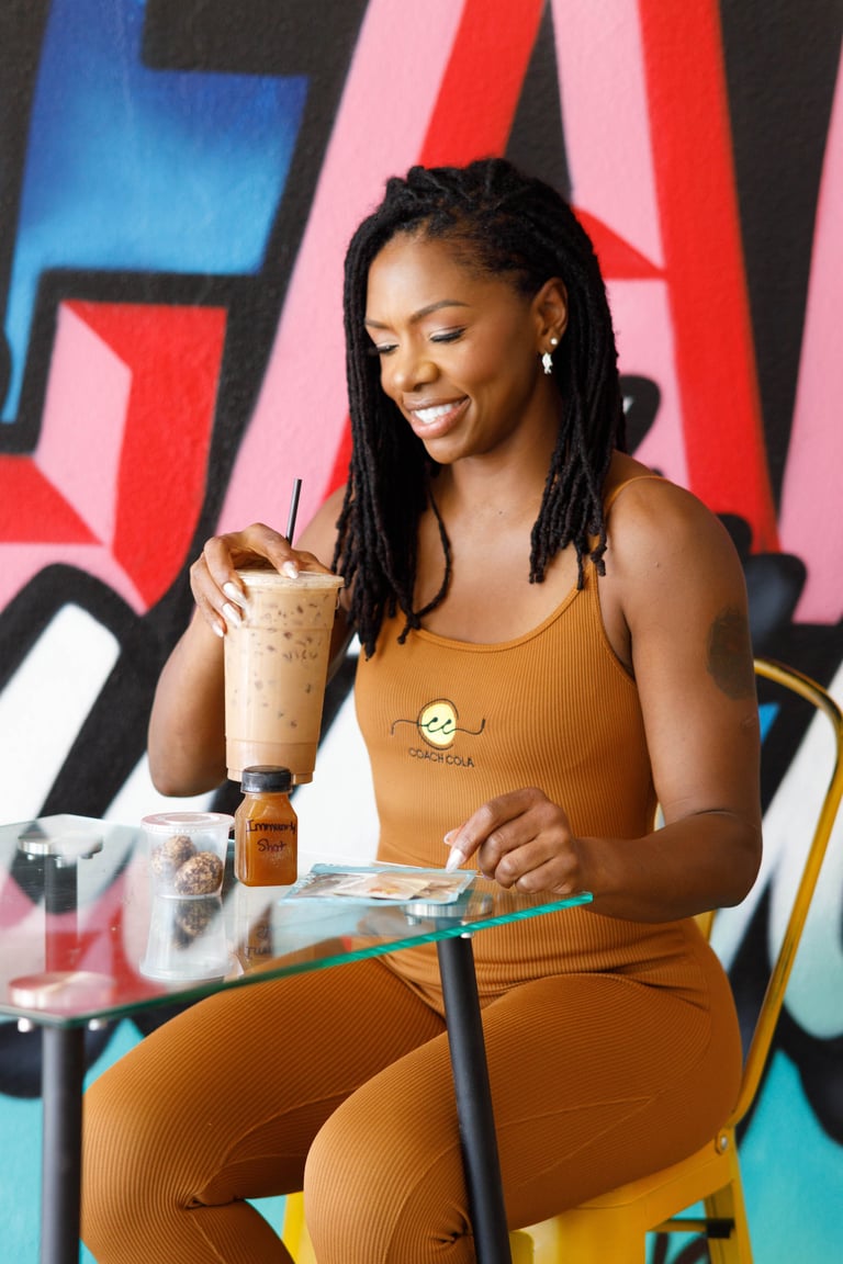 Woman in tan outfit holding iced beverage with straw sitting against colorful street art mural background