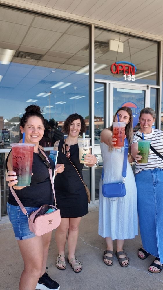 Four smiling women holding colorful drinks standing outside Duncanville Nutrition storefront