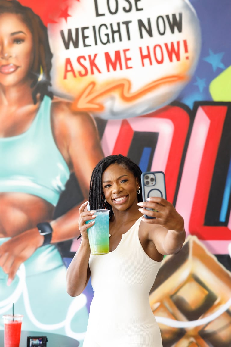 Woman in white tank top holding a green smoothie taking a selfie in front of weight loss promotion billboard