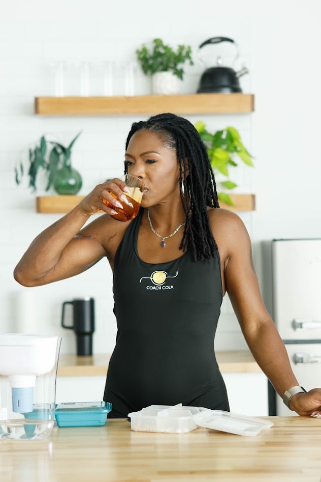 Woman in black tank top eating a snack at wooden table in bright kitchen